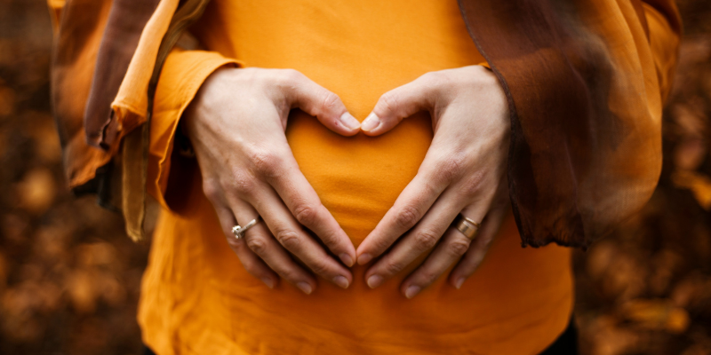 Pregnant women in yellow shirt making a heart sign with her hands on her stomach
