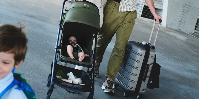 Dad pushing baby in airport in Bugaboo Butterfly 2 with one hand and suitcase in the other