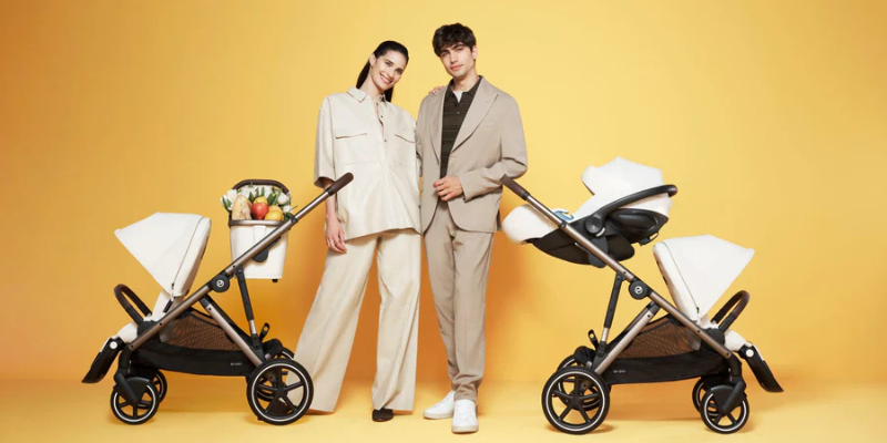 Parents standing with two Cybex Gazelle S Strollers. One of the strollers has the basket attached and one has a car seat
