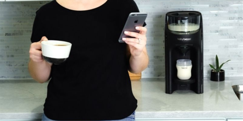 Woman Looking at Phone While Using the Baby Brezza Formula Pro Advanced Wifi