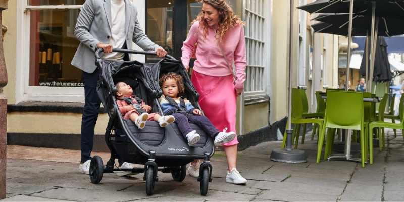 Man and Woman Pushing Baby Jogger City Mini GT2 Double Stroller With Two Toddlers Sitting Inside