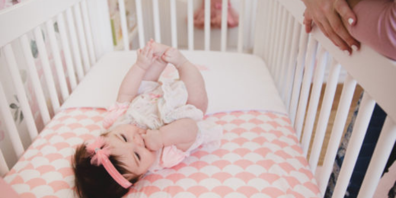 Baby Lying in Crib With Pink Checkered Sheets