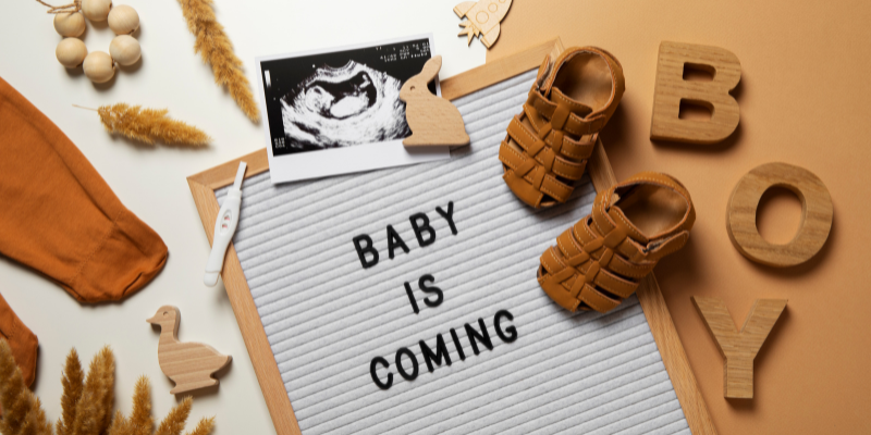 sign that says baby is coming with little shoes and picture of sonograph 