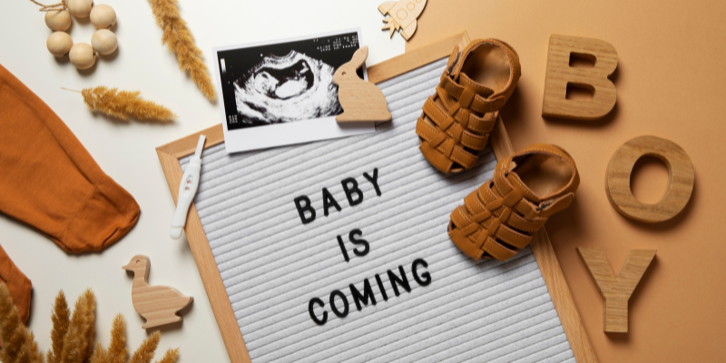 sign that says baby is coming with little shoes and picture of sonograph