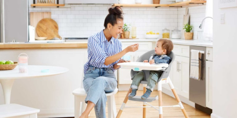 Woman Feeding Child Sitting in Skip Hop EON 4-in-1 Multi-Stage High Chair