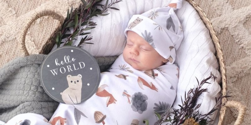 Baby Lying in Basket Wrapped in Blanket With a Hello World Tag Beside Him