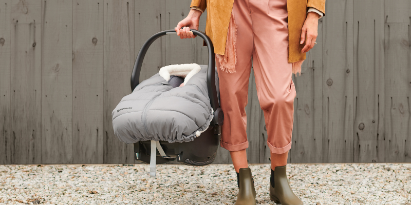 Mother holding an UPPAbaby MESA V2 Infant Seat in a Cozyganoosh car seat cover
