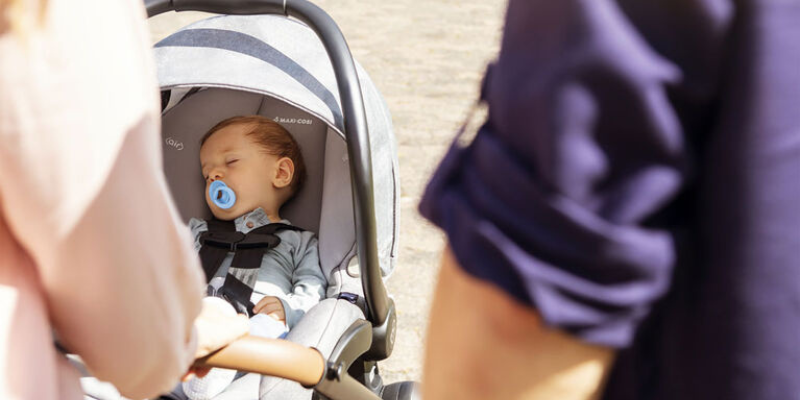 Parents watching over a baby sitting in a Maxi-Cosi car seat