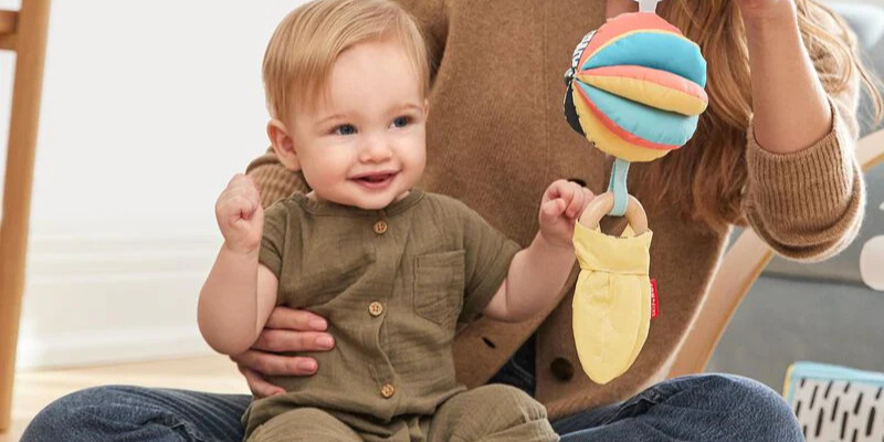 Toddler on mother's lap playing with Skip Hop Stroller Toy
