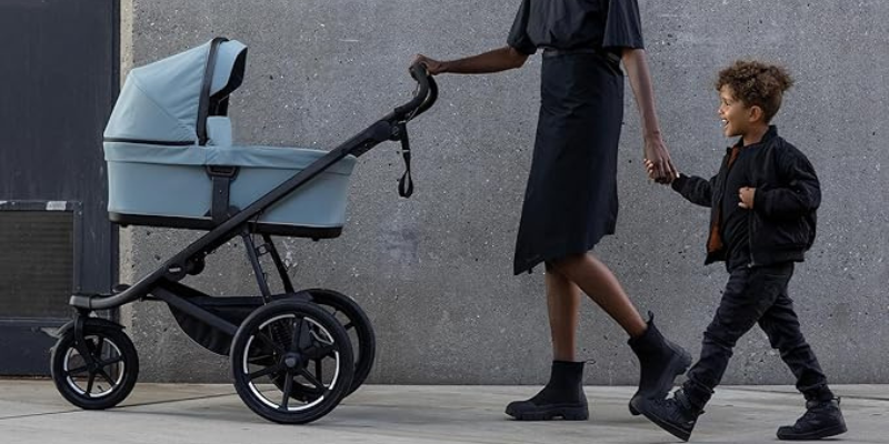 Mom with little brother pushing Thule Urban Glide 3 stroller with bassinet accessory attached