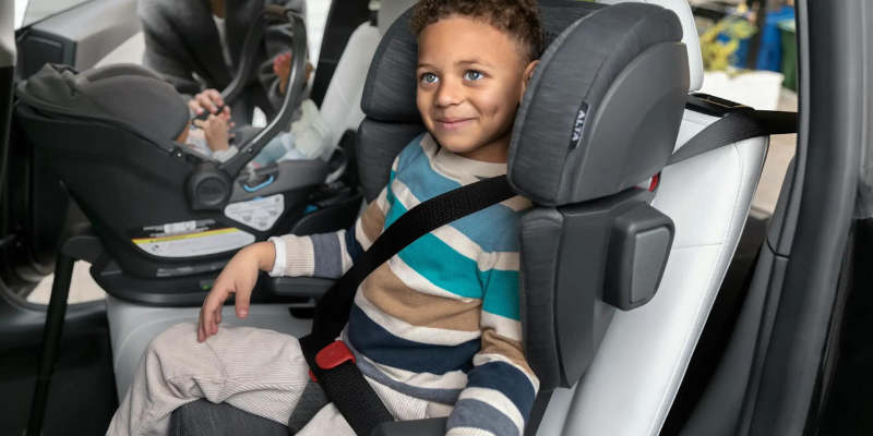 Little boy sitting in a booster seat beside sibling in an infant car seat