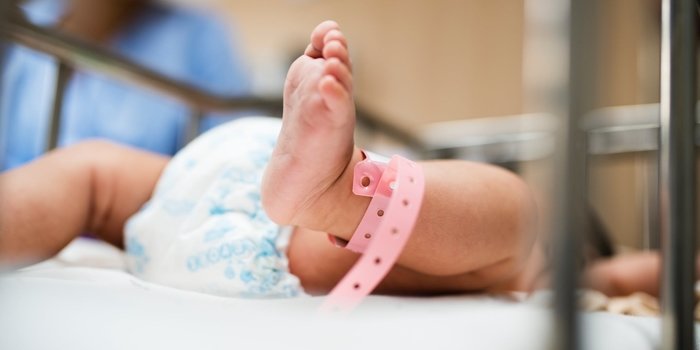 Image of a newborns foot, in the hospital, wearing a pink hospital bracelet around its ankle