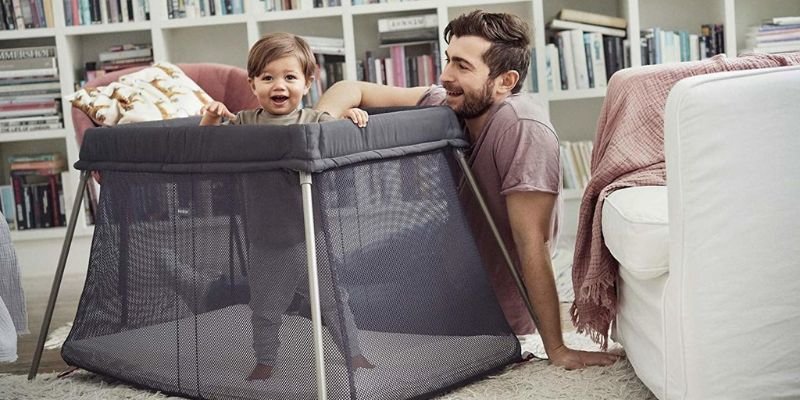 Baby standing in Baby Bjorn Play Yard Light and dad sitting on floor