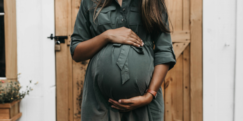 Woman in green dress holding pregnant belly