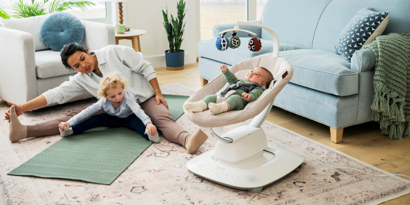 Mom and toddler doing yoga on matt while baby plays in UPPAbaby Mamaroo Smart Swing