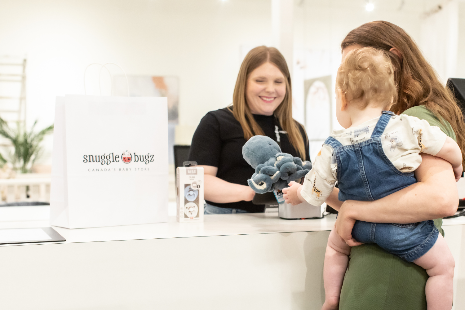 Women shopping in Snuggle Bugz store with child, at checkout buying baby items
