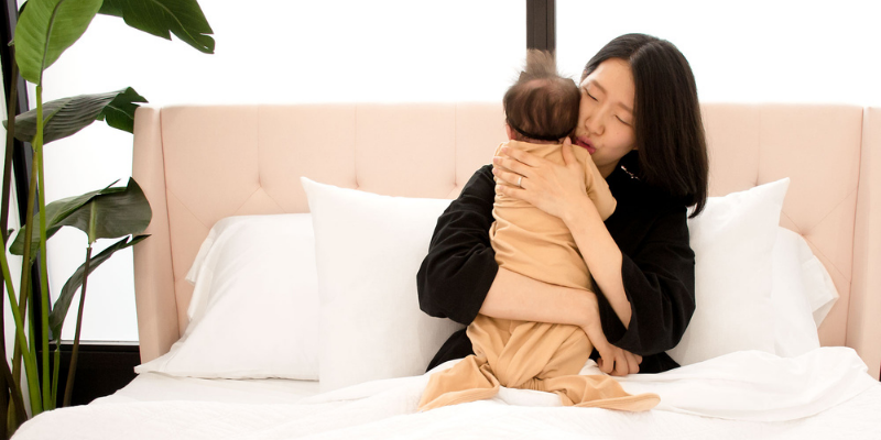 Mother holding and calming baby while sitting in bed