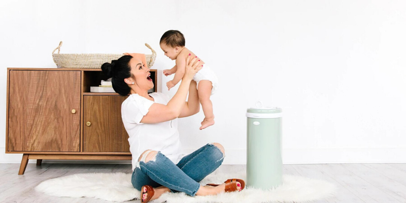 Woman holding baby in the air with diaper pail sitting beside them