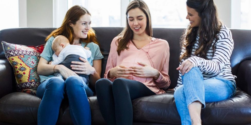 Pregnant woman smiling with two friends on couch