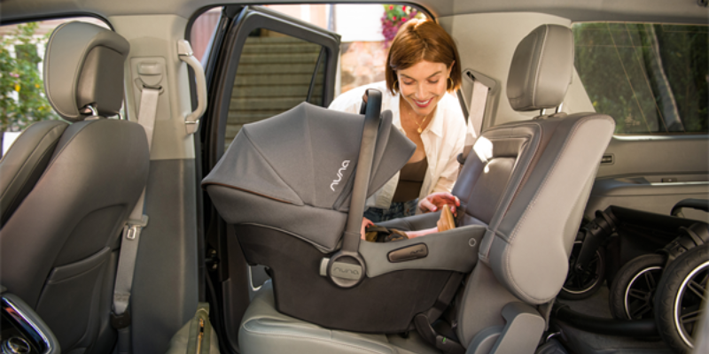 Woman installing Nuna Urbn Infant car seat in the back seat of vehicle