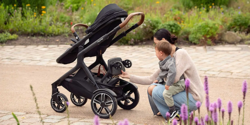 Mom holding child & putting away a Rider Board into a Nuna DEMI Next Stroller