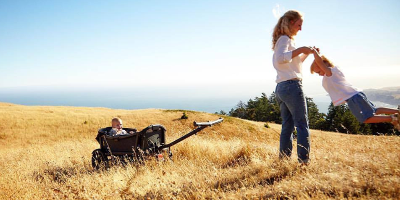 Woman swinging child in a field, the Veer all-terrain cruiser in the backgrounf