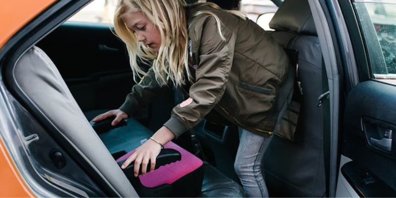 Clek Olli Booster Seat Being Put in Back of Car by Little Girl