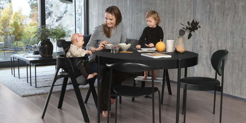 Woman Sitting at Table With Toddler and Baby Sitting in Stokke Steps High Chair