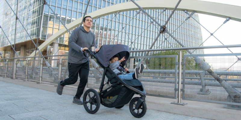 Man Jogging with BOB Wayfinder Stroller in Grey with Baby Sitting Inside. 