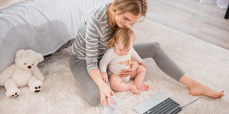 Woman Sitting on Floor Holding Baby While Looking At Computer