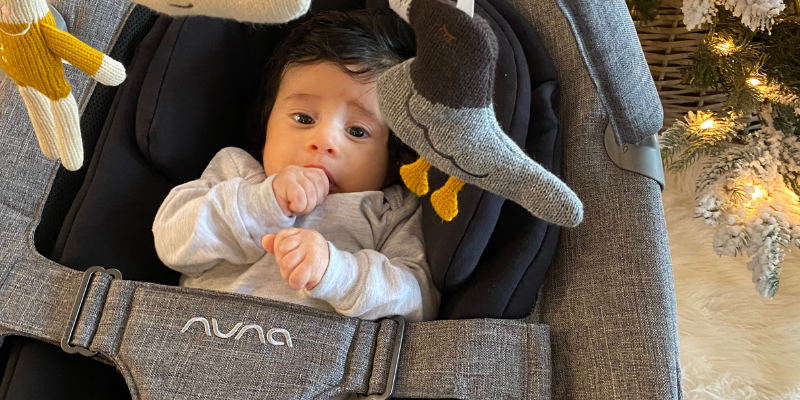 Baby sucking their thumb and in a Nuna Leaf Grow Swing