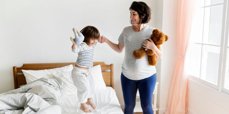Mom holding toddlers hand as she jumps on a bed