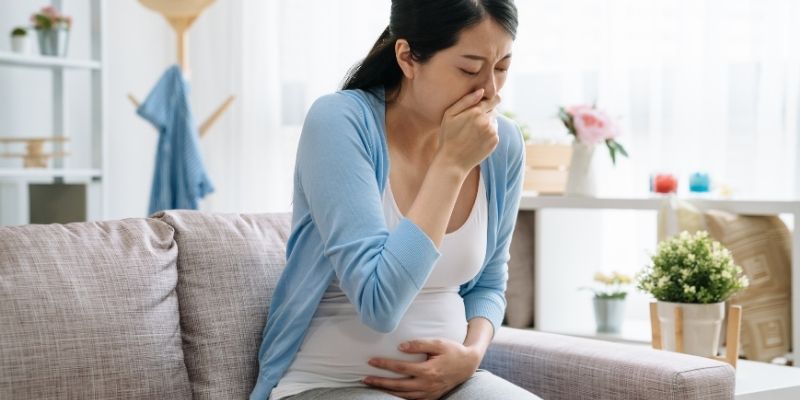 Pregnant woman feeling morning sickness, holding stomach and resting on couch, early pregnancy nausea relief concept