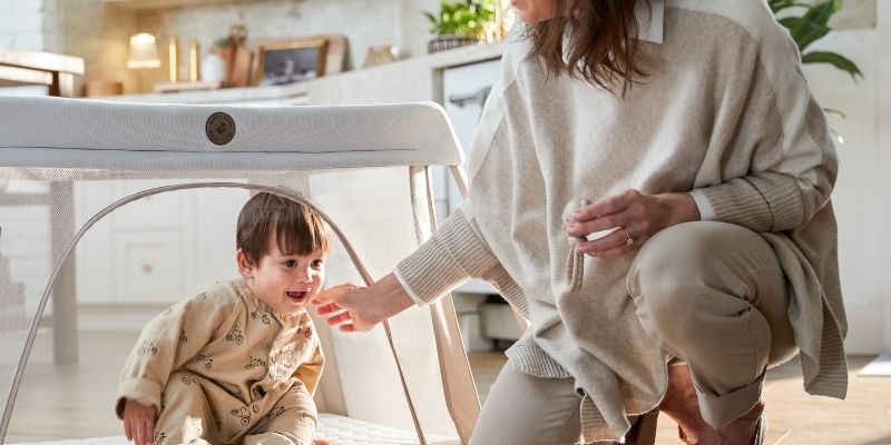 Little boy sitting in a Maxi-Cosi playard with grandma in the kitchen