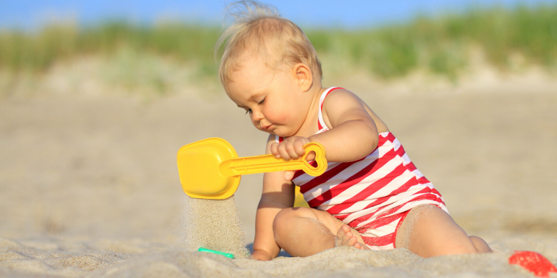 baby playing with sand and plastic shovel on beach