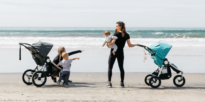 Two women with their infant and toddlers, on a beach, looking at the ocean with their Bumbleride Strollers