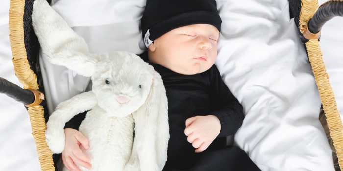 Baby in black outfit, sleeping in a bassinet and holding a stuffed bunny