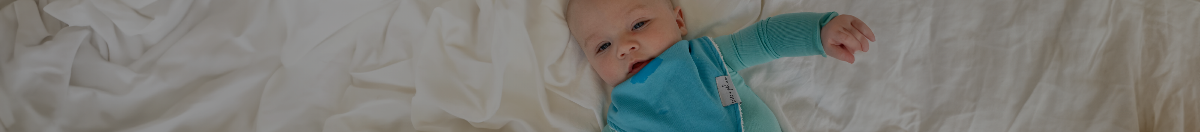 Baby laying on bed wearing a blue Pip + Phee sleeper and matching bib