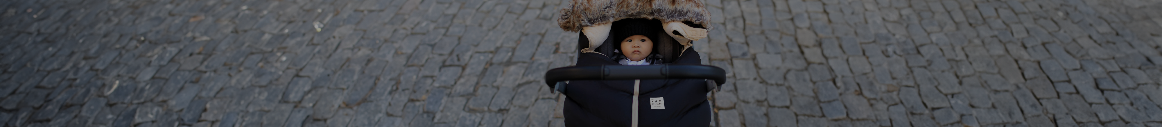 Mom pushing stroller down cobblestone road with infant in car seat cover