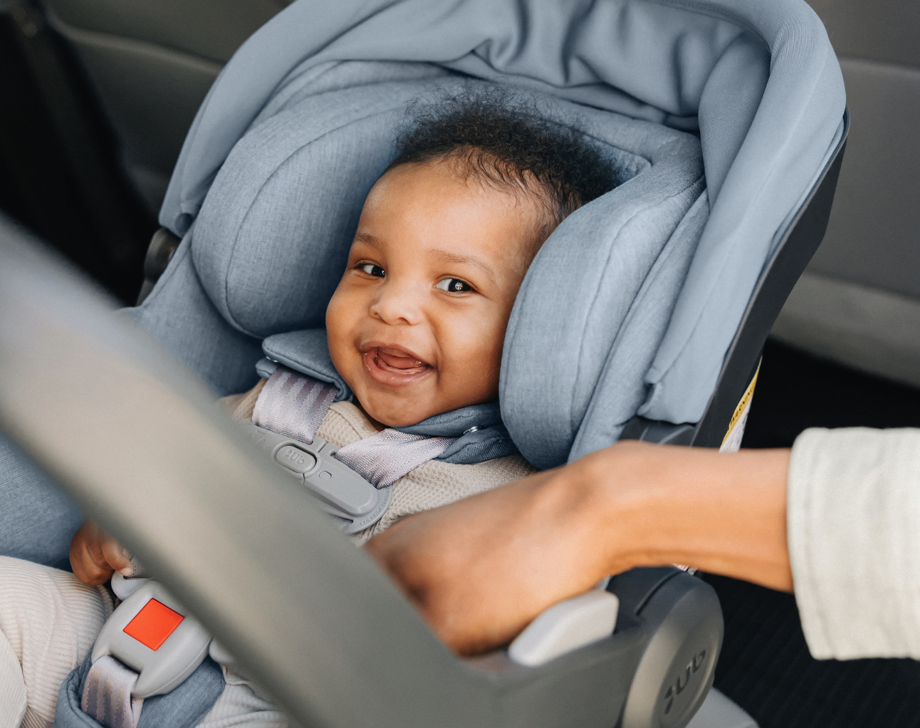 Baby sitting in an UPPAbaby MESA V2 infant car seat, smiling